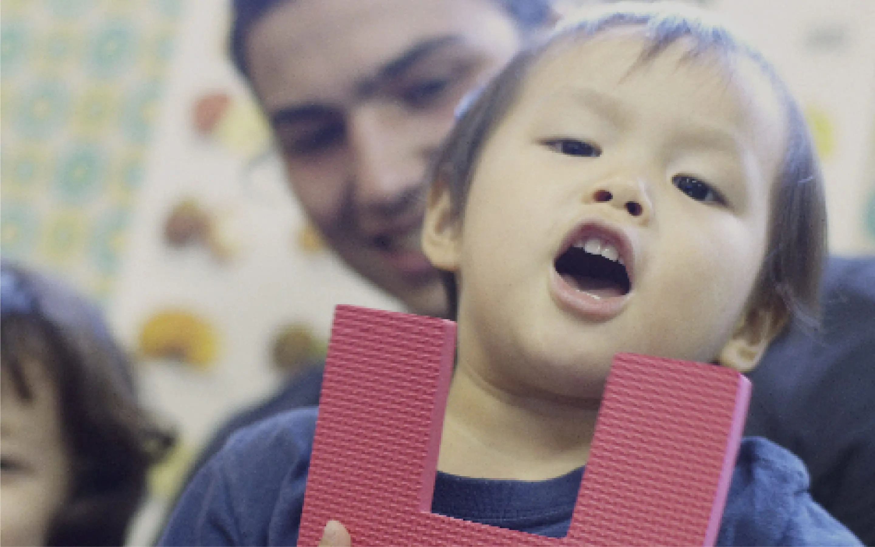 先生と園児が教室で楽しくアルファベットブロックを持って遊んでいる様子